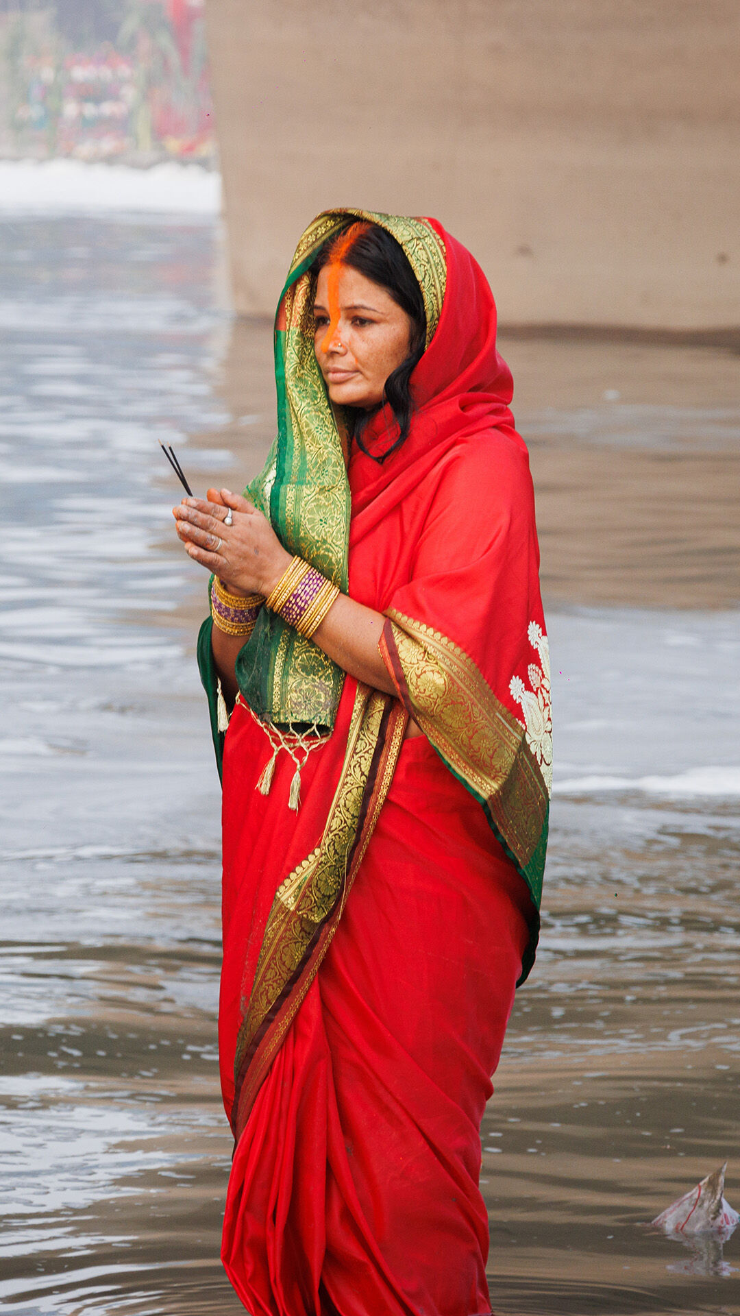 A woman in a red saree performing the solemn water ritual during the Chhath Puja worship.